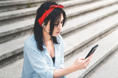 Young woman using phone while sitting on staircase