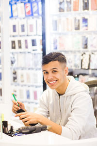 Portrait of smiling teenage trainee repairing mobile phone while sitting at illuminated desk in store