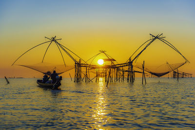 Silhouette fishing net on sea against sky during sunset