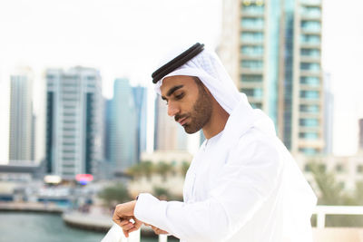 Side view of young man standing against buildings in city