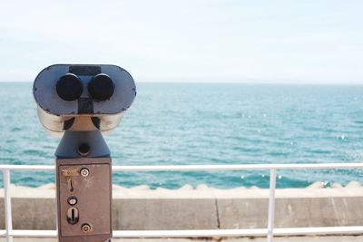 Coin-operated binoculars by sea against sky