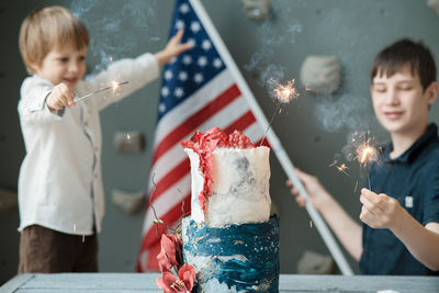 Smiling kids holding american flag and lighted sparklers at independence day celebration