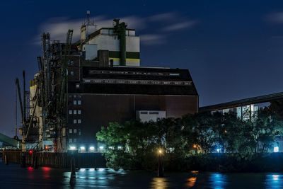 Buildings by river against sky at night