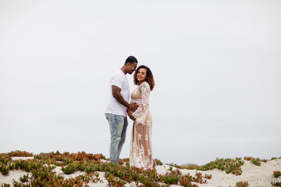 Mixed race couple embracing on sand dunes maternity