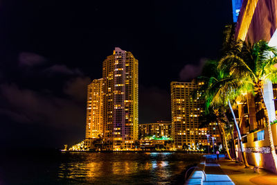 Illuminated buildings by sea against sky at night