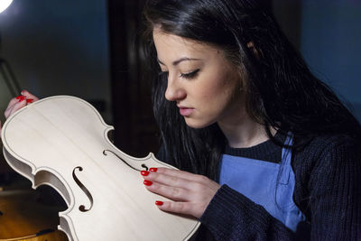 Young woman apprentice violinmaker checking the beauty of her violin