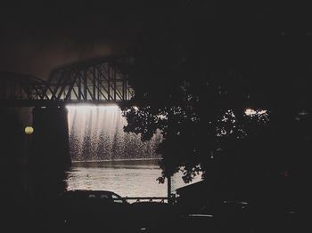 Silhouette trees by river against sky at night