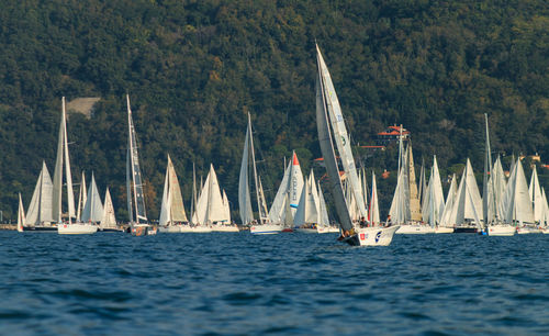 Sailboats sailing on sea by mountains against sky