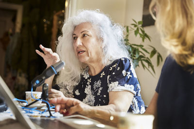 Senior woman talking on microphone while sitting with friend at table