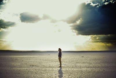 Full length side view of man standing at salt lake against sky during sunset