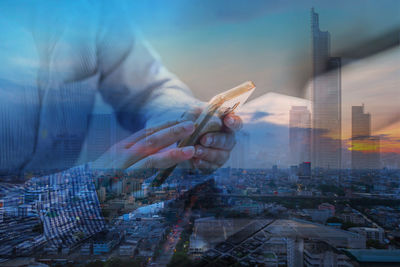 Digital composite image of hand using mobile phone with modern buildings in city