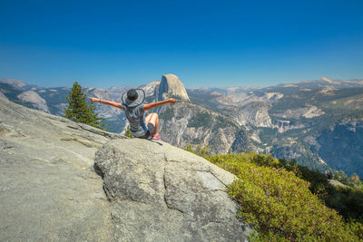 Rear view of people on rocks by mountains against blue sky