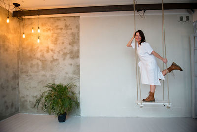 Portrait of woman standing on swing in illuminated room