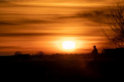 Silhouette man standing on field against orange sky