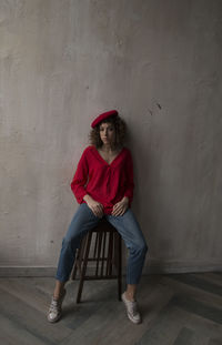 Full length portrait of woman sitting against wall