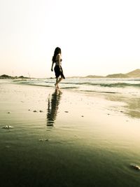 Young woman standing on beach against clear sky