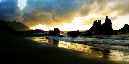 Silhouette rocks on beach against sky during sunset