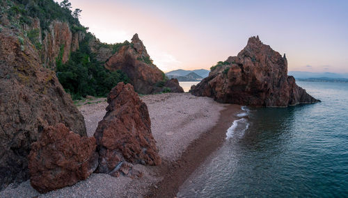 Rock formations on shore against sky during sunset