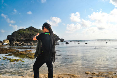 Rear view of man standing at beach against sky