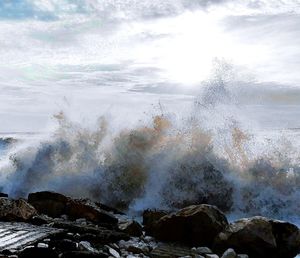 Water splashing on rocks against sky