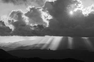 Sunlight streaming through clouds over silhouette mountains
