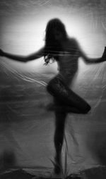 Silhouette woman posing while standing behind curtain in dark room