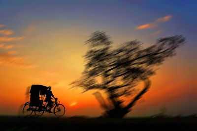 Silhouette person riding bicycle against sky during sunset