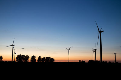 Silhouette wind turbines on field against clear sky during sunset