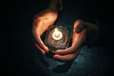 Cropped hands with illuminated candle in darkroom