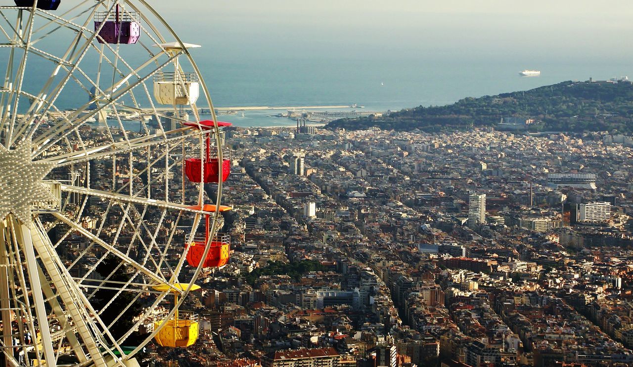 architecture, sea, ferris wheel, built structure, building exterior, amusement park, amusement park ride, city, water, cityscape, sky, nautical vessel, high angle view, transportation, mode of transport, horizon over water, travel, outdoors, travel destinations, arts culture and entertainment