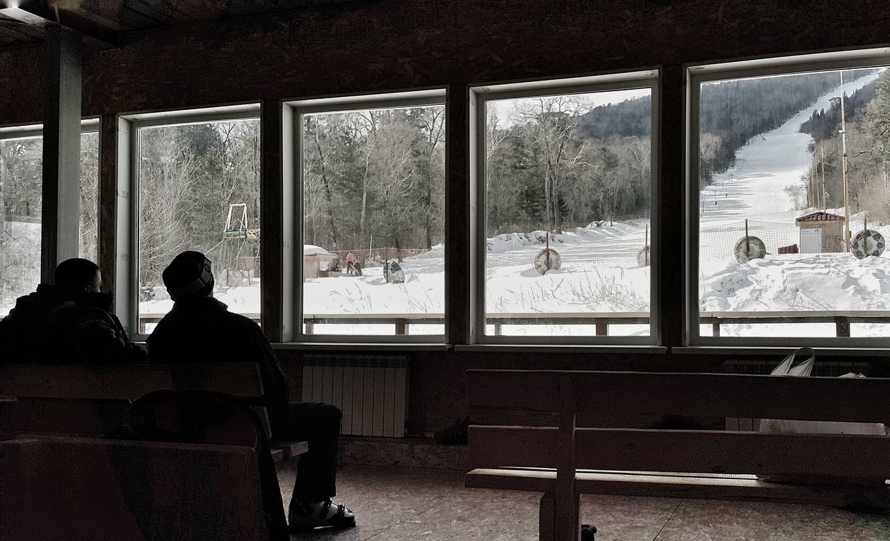 indoors, window, men, architecture, sitting, built structure, lifestyles, leisure activity, person, rear view, glass - material, silhouette, day, building exterior, sunlight, standing, transparent