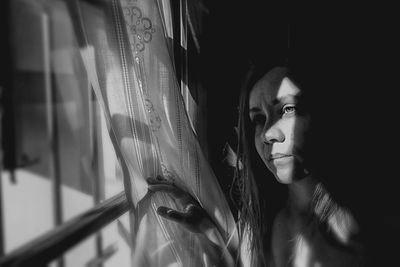 Portrait of young woman looking through window at home