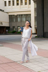 Middle-aged woman dressed in jacket and trousers walks around city against