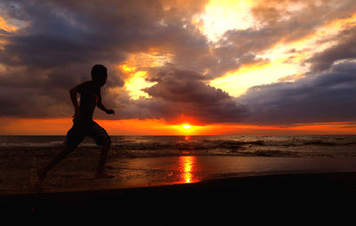 Silhouette man on beach against sky during sunset