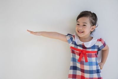 Smiling girl gesturing while standing against wall