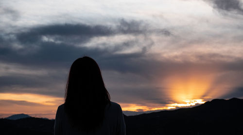 Rear view of silhouette woman standing against sky during sunset