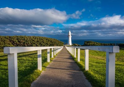 Footpath amidst field leading to cape otway lighthouse against cloudy sky