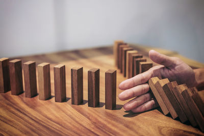 Cropped hand of person blocking wooden dominoes on table