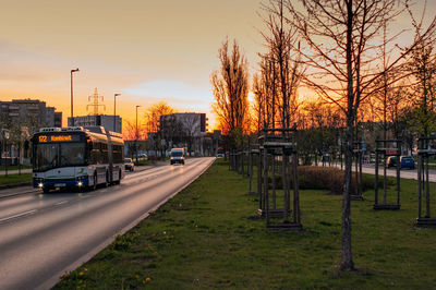 Road by bare trees against sky during sunset