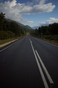 Empty road by trees against sky