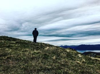 Man standing on cliff against cloudy sky