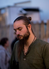 Close-up of young man looking down while standing outdoors at sunset