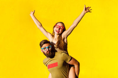 Man carrying woman on back against yellow background