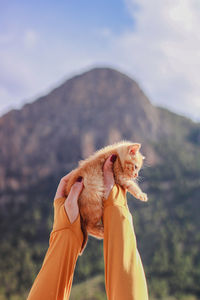 Cropped hand of woman with dog against sky