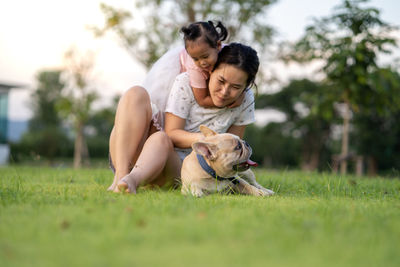 Woman piggybacking girl with dog on grass