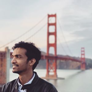 Smiling young man standing against golden gate bridge against sky