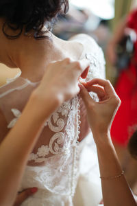 Cropped hands of woman helping bride in dressing