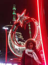 Portrait of smiling young woman standing in amusement park at night