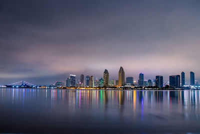 Illuminated modern buildings by bay against sky