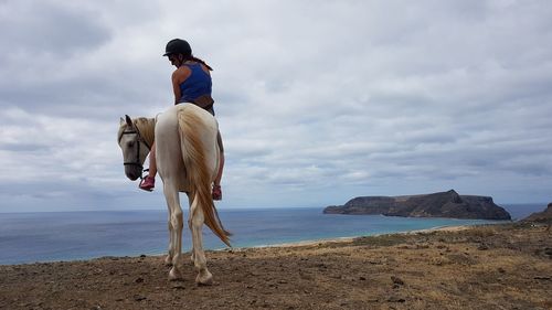 Woman riding horse on cliff above beach 